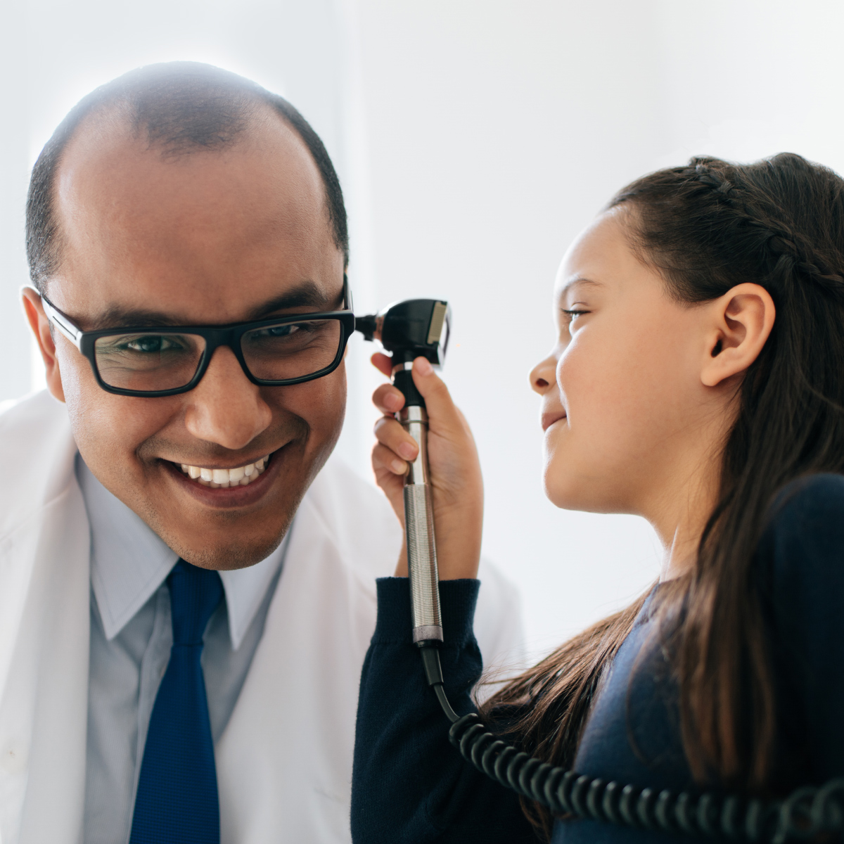 male doctor smiling as young female patient looks in his ear