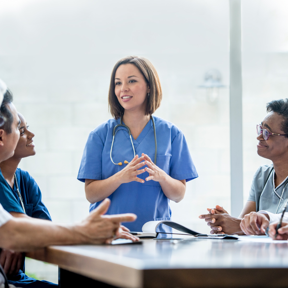 smiling female doctor addressing other doctors around a table