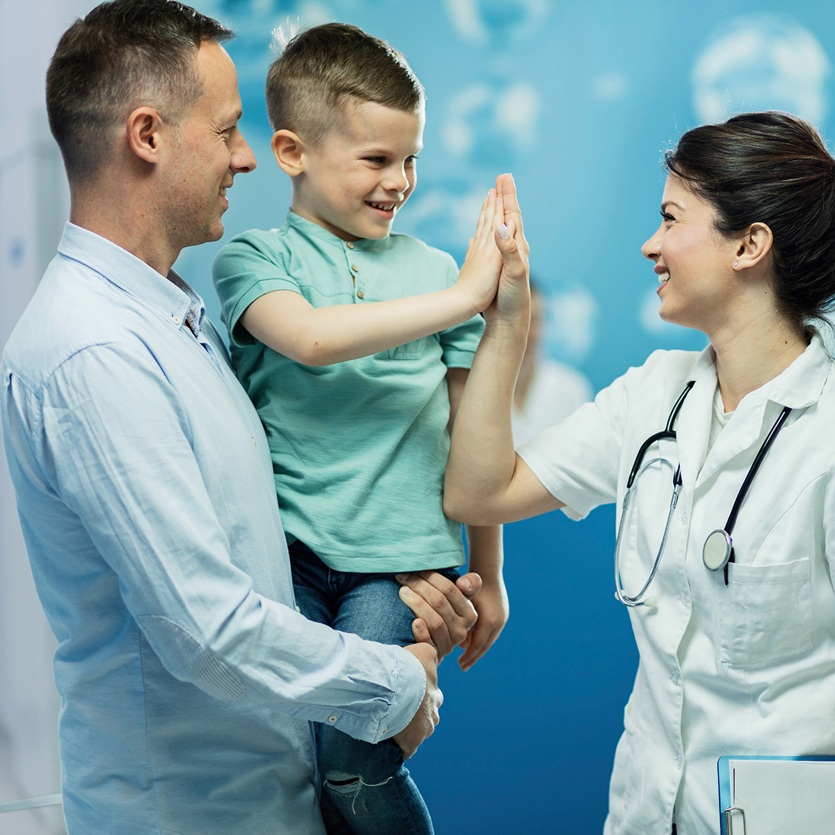 smiling young male patient being held by smiling father gives a high-five to a smiling female doctor