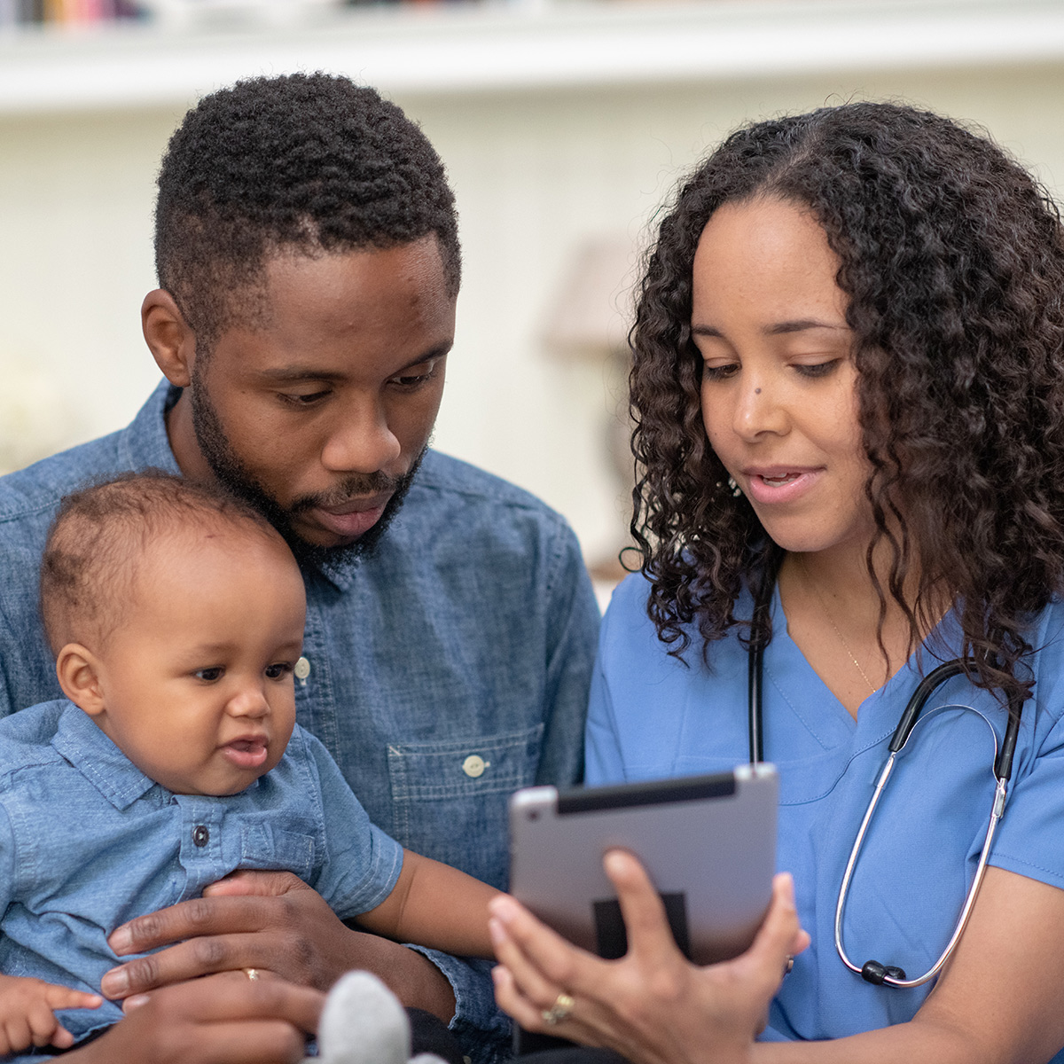 female technician in scrubs showing notes on a tablet to father holding infant