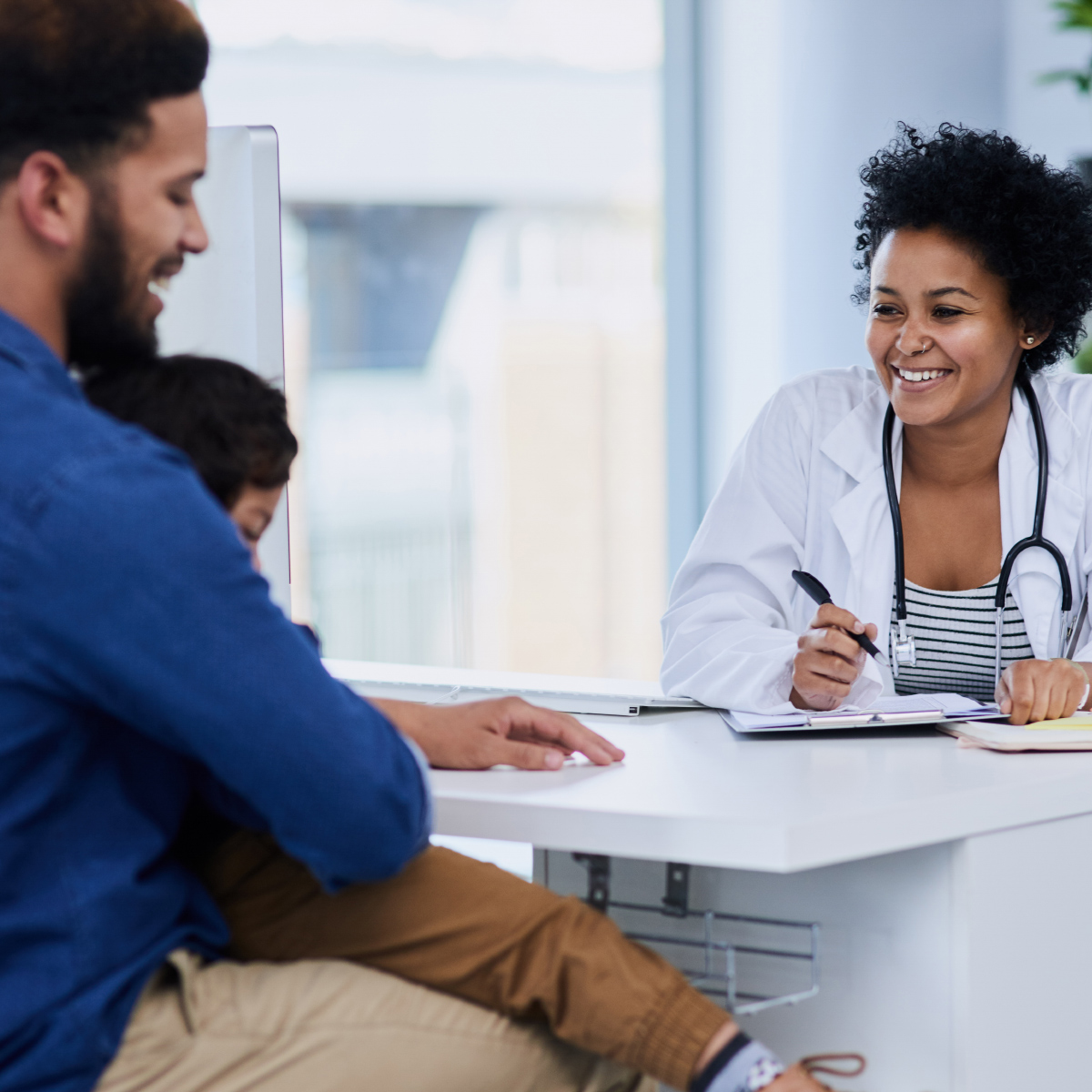 female doctor smiling at young patient held by smiling father